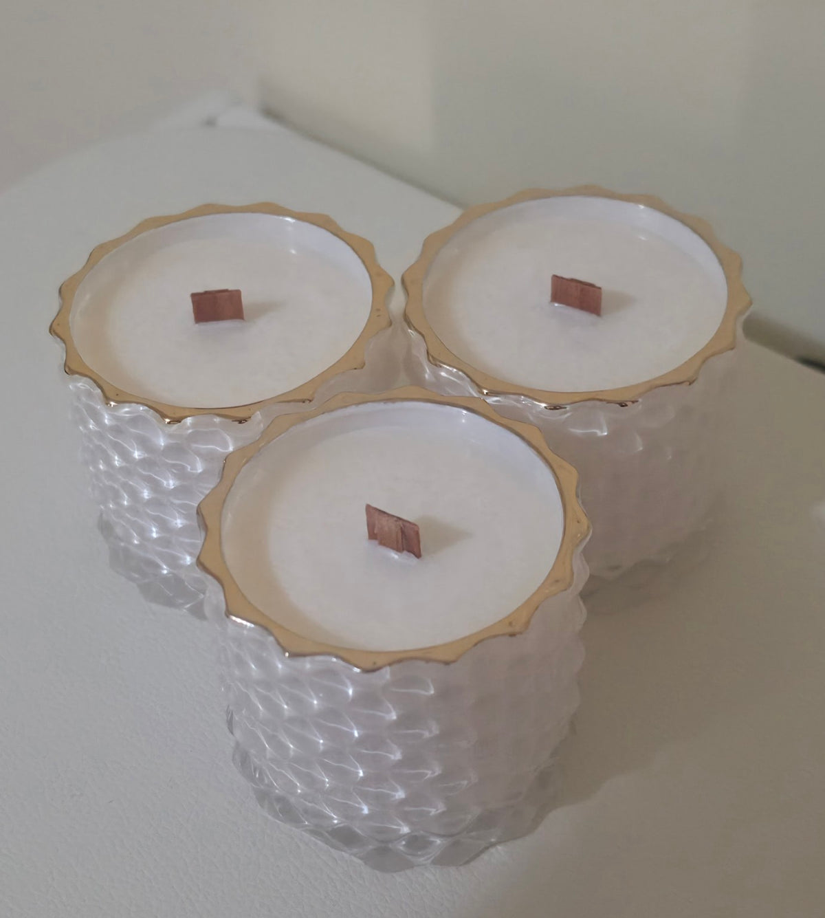 Three Serenus Spa Luxe cocosoy candles in white geometric jars with gold rims and wooden wicks.